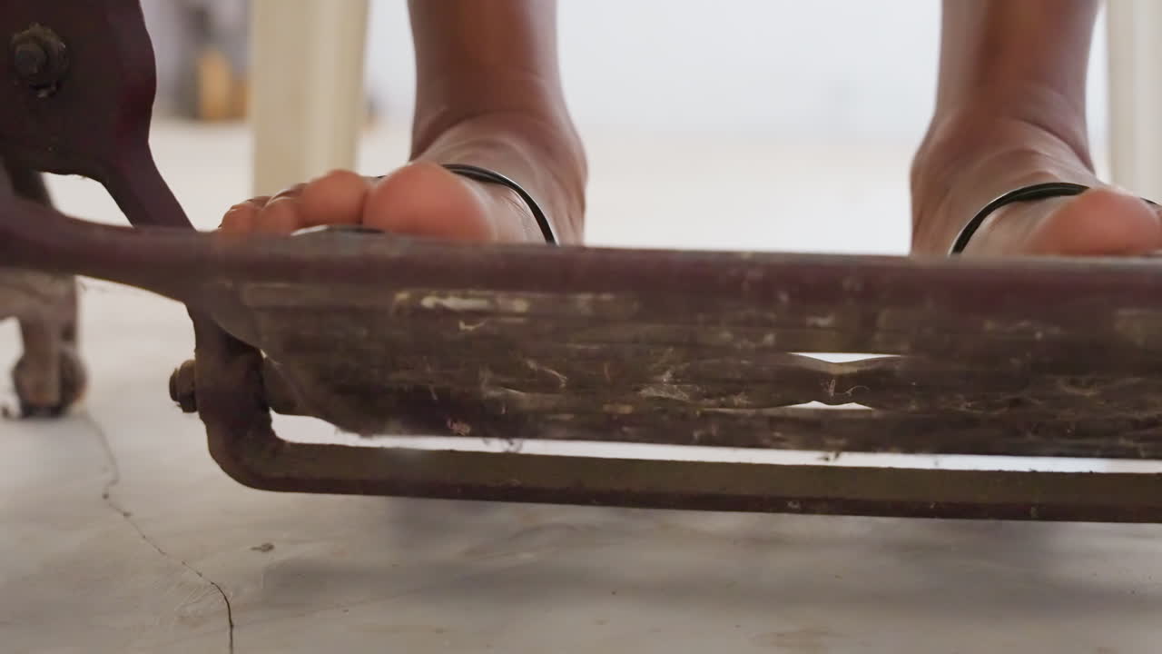 Closeup toes pressing black treadle pedal on house floor, sandal shifting on metal grate, deliberate press and release motion, close rhythm for mending or tailoring, intimate workshop to home vibe