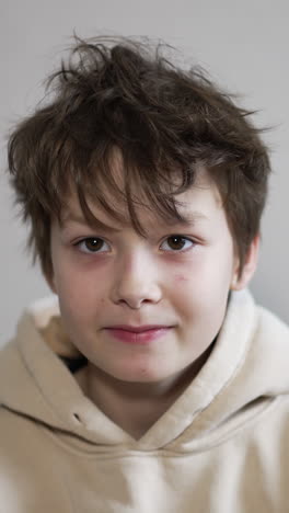 handsome caucasian boy posing in front of camera. kid puts his hands on face, rubs his eyes and then stretches arms to the sides lazily. vertical video