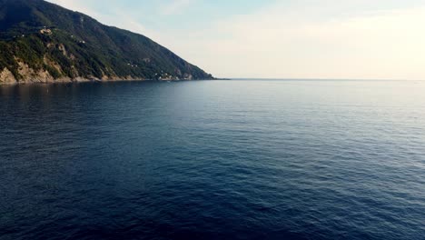 blue ocean water with smooth waves under mountain of camogli coast, genova, italy