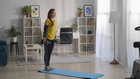 una mujer joven está haciendo sentadillas con pesas en las manos entrenando sola en la sala de estar de un apartamento moderno ejercicios para una buena figura