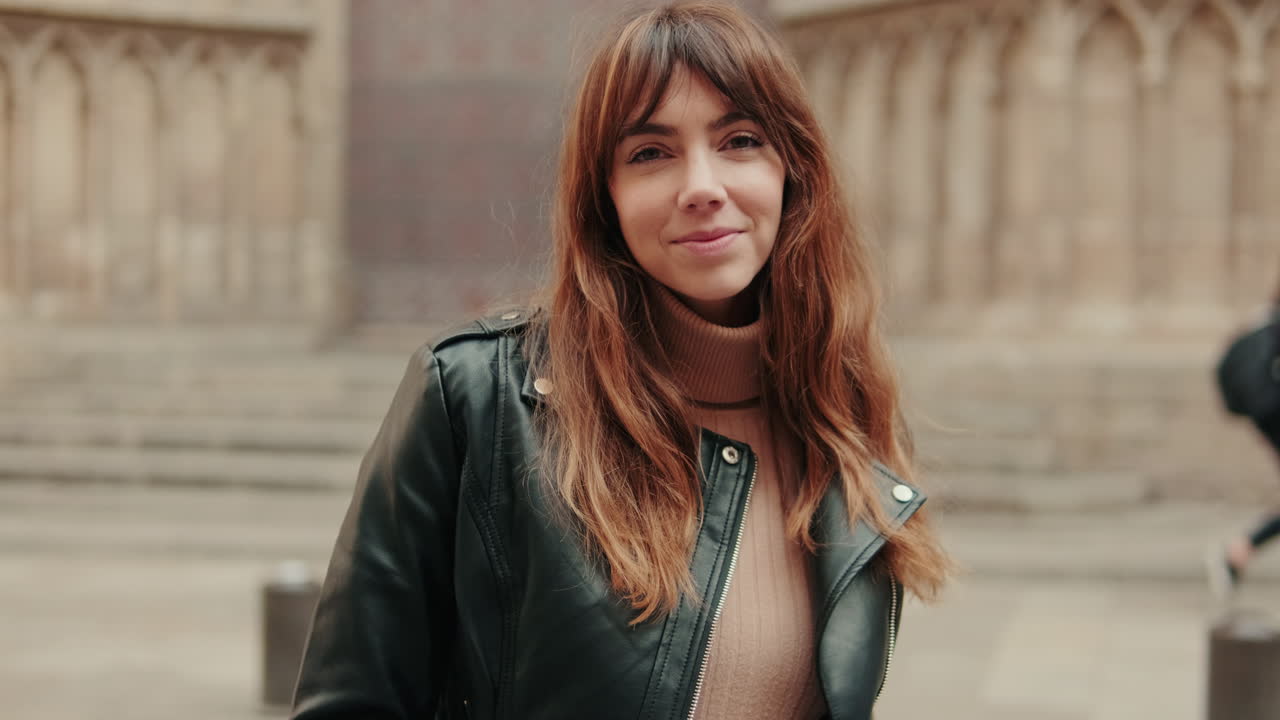 Mujer joven sonriente con chaqueta de cuero mirando a cámara al aire libre