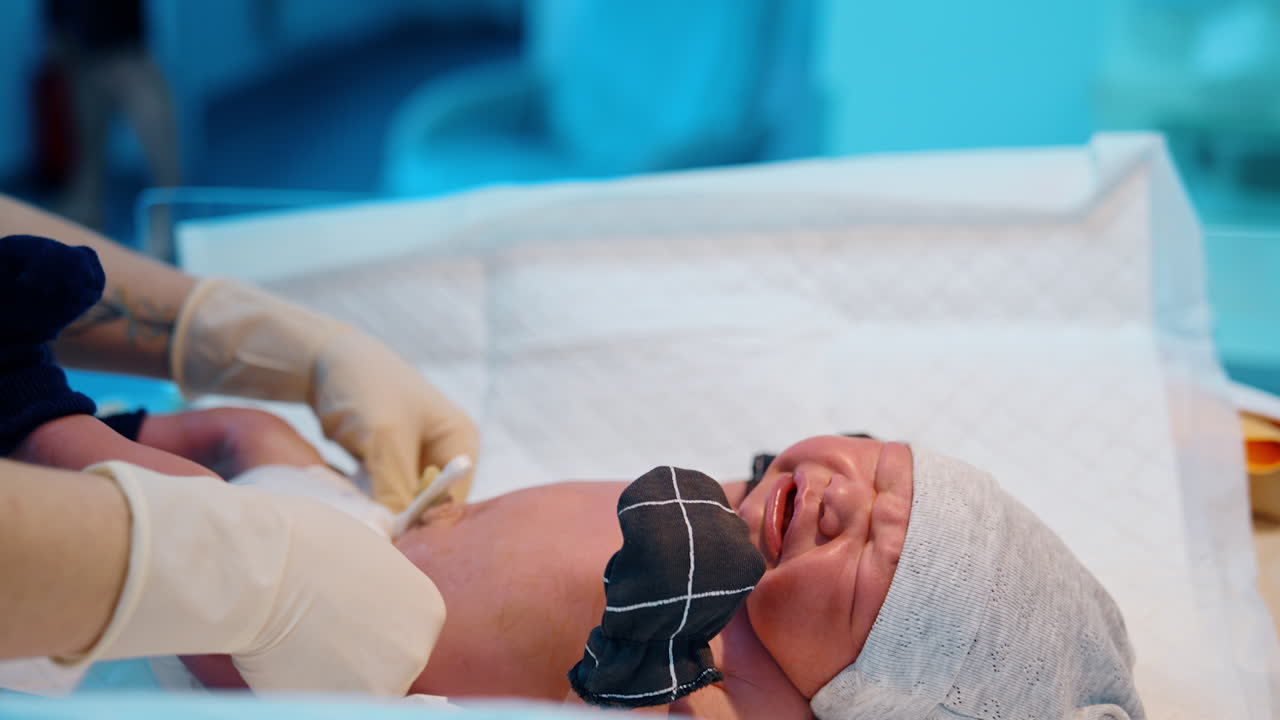 Just born infant crying bitterly on the table. Newborn baby is dressed in a cap, mittens, socks and diaper.