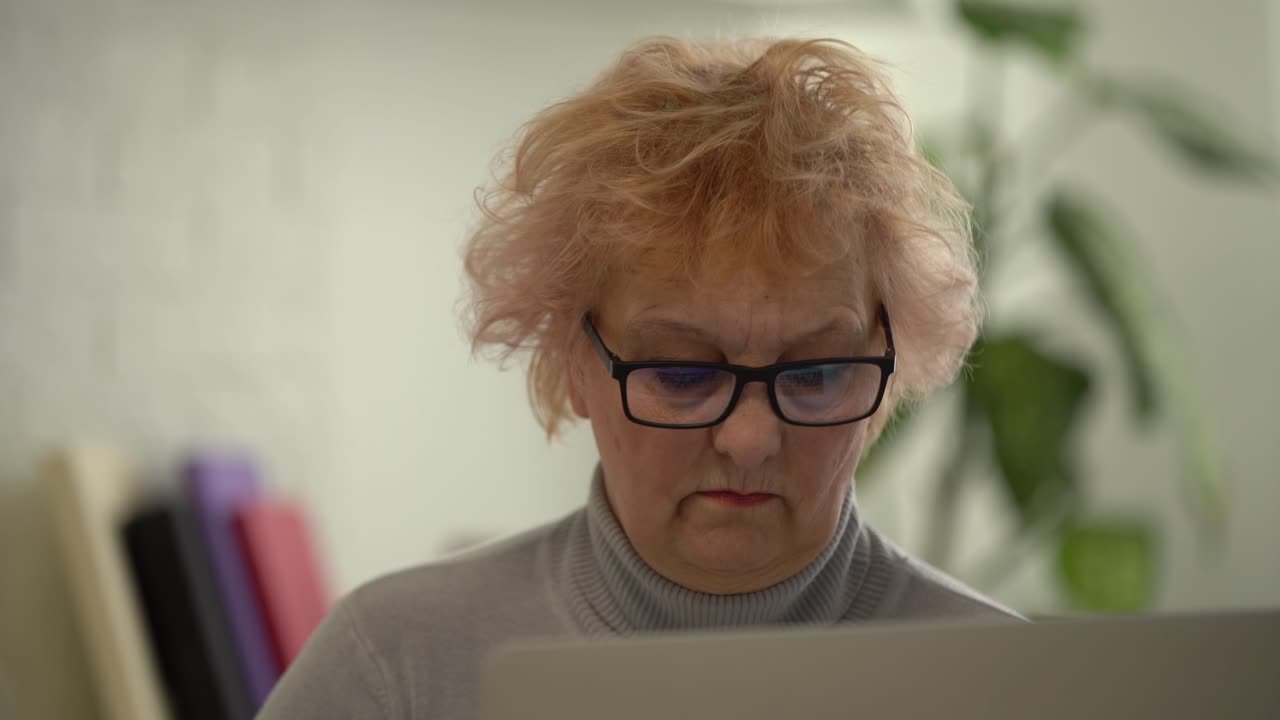 Elderly working on laptop at home. Portrait of senior businesswoman having phone call and working on computer remotely at home