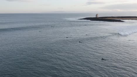 Aerial-of-surfers-swimming-towards-lineup-area-behind-break,-duckdiving