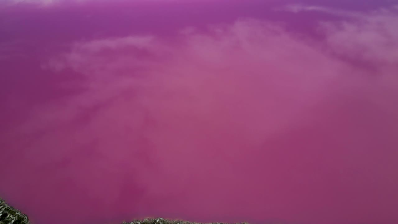 Aerial view from drone overhead Hutt Lagoon Pink Lake, tilting upwards to distant view towards Indian Ocean, clouds reflected on the pink lake surface