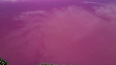 Aerial-view-from-drone-overhead-Hutt-Lagoon-Pink-Lake,-tilting-upwards-to-distant-view-towards-Indian-Ocean,-clouds-reflected-on-the-pink-lake-surface