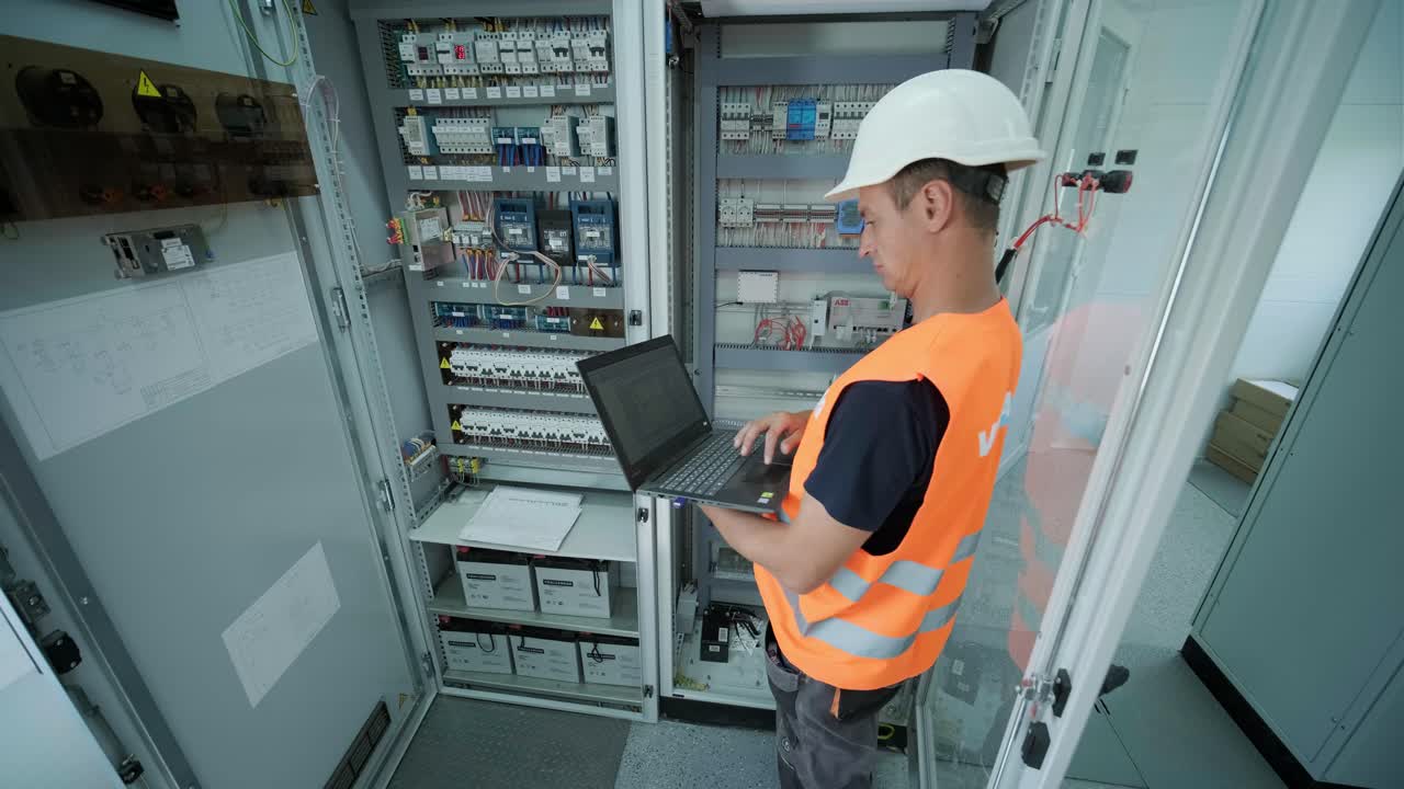 el ingeniero eléctrico que trabaja comprueba la tensión de corriente eléctrica y la sobrecarga frente al gabinete del centro de carga o la unidad de consumo para el mantenimiento con un portátil en la sala principal del sistema de distribución de energía.
