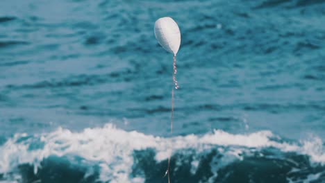 Weißer-Heliumballon-In-Form-Eines-Herzens,-Der-Vor-Dem-Meer-Aufsteigt