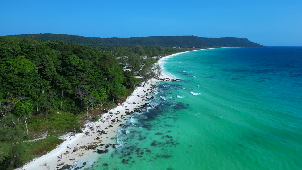 Black Stones in turquoise water gently washing the white sand beach of Koh Rong island, cambodia, on a sunny day with clear blue sky. Lovely aerial view flight fly push forward drone