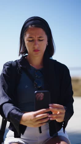 Vertical-shot-of-woman-hold-and-scroll-smartphone-while-squat,-Mallorca