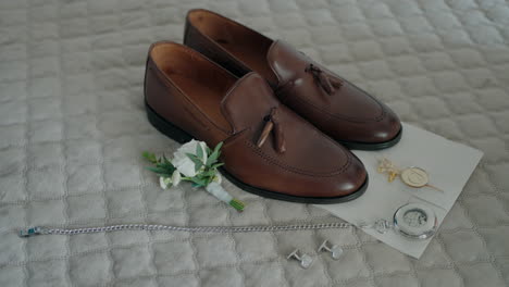 groom's wedding accessories including brown shoes, boutonniere, pocket watch, bracelet, cufflinks, and envelope, arranged neatly