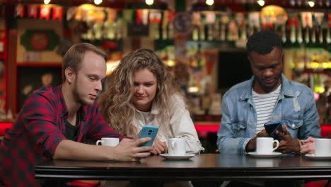 group of friends at a bar drinking coffee and discussing while looking at the screen of a smartphone.