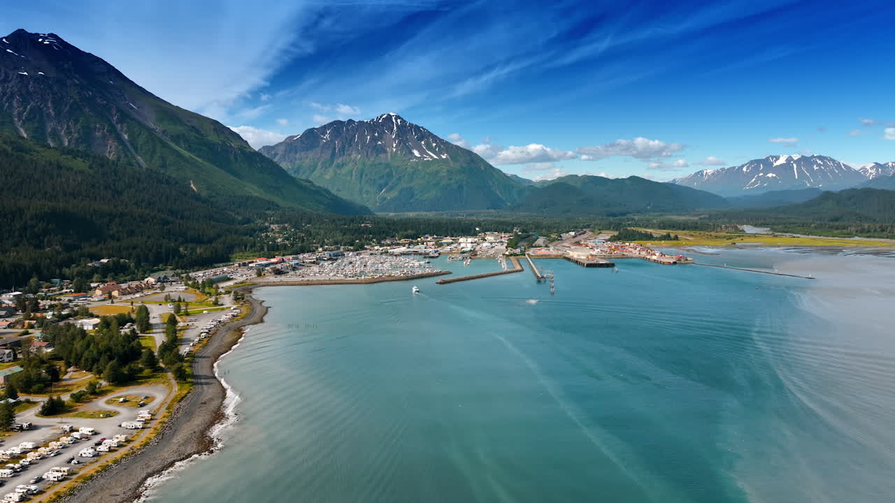 Flyvning over søens blå vandlandskab nær byen beliggende ved den smukke vandfront. Stedsegrønne skove og fantastiske bjerge omgiver byområdet. Alaska, luftfoto
