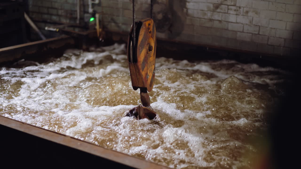 Frothy turbulent water in industrial quenching tank with crane hook, steamy atmosphere