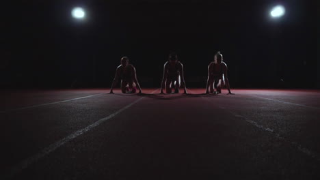 three girls in black clothes are in the starting pads to start the race in the competition in the light of the lights and run towards the finish