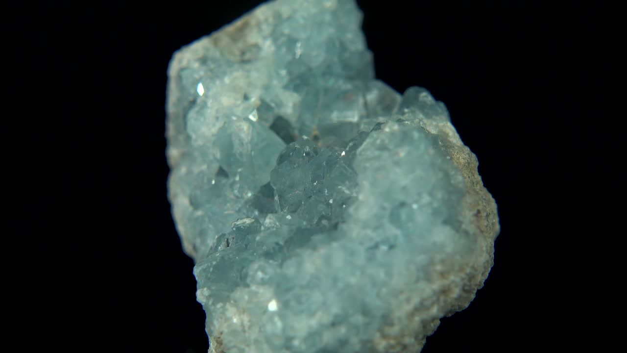 검은색 배경 앞에 밝은 파란색 미네랄 (셀레스틴) 을 원활하게 회전시니다.