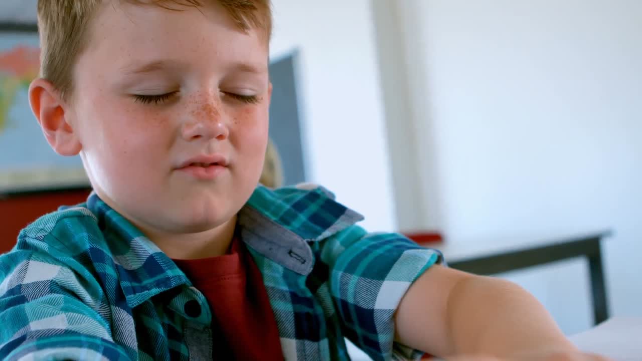 Escolar caucásico ciego leyendo un libro en braille en un pupitre en el aula de la escuela 4k
