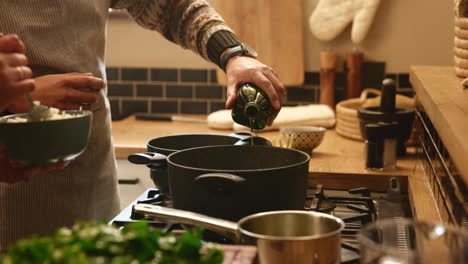 a person pouring oil into a pot on the stove in a kitchen