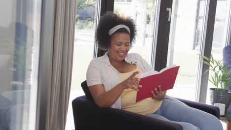 mujer afroamericana de tamaño grande sentada en un sillón y leyendo un libro, inalterada, en cámara lenta