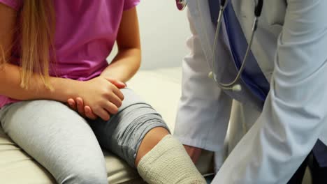 Female-doctor-putting-bandage-on-injured-leg-of-girl