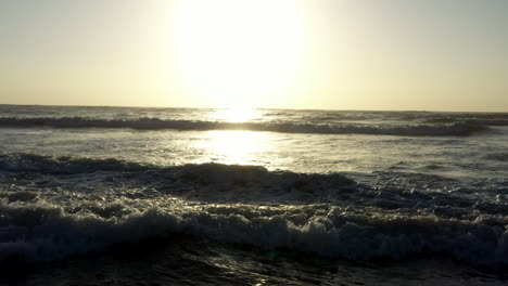 aerial golden sunrise low over crashing ocean waves