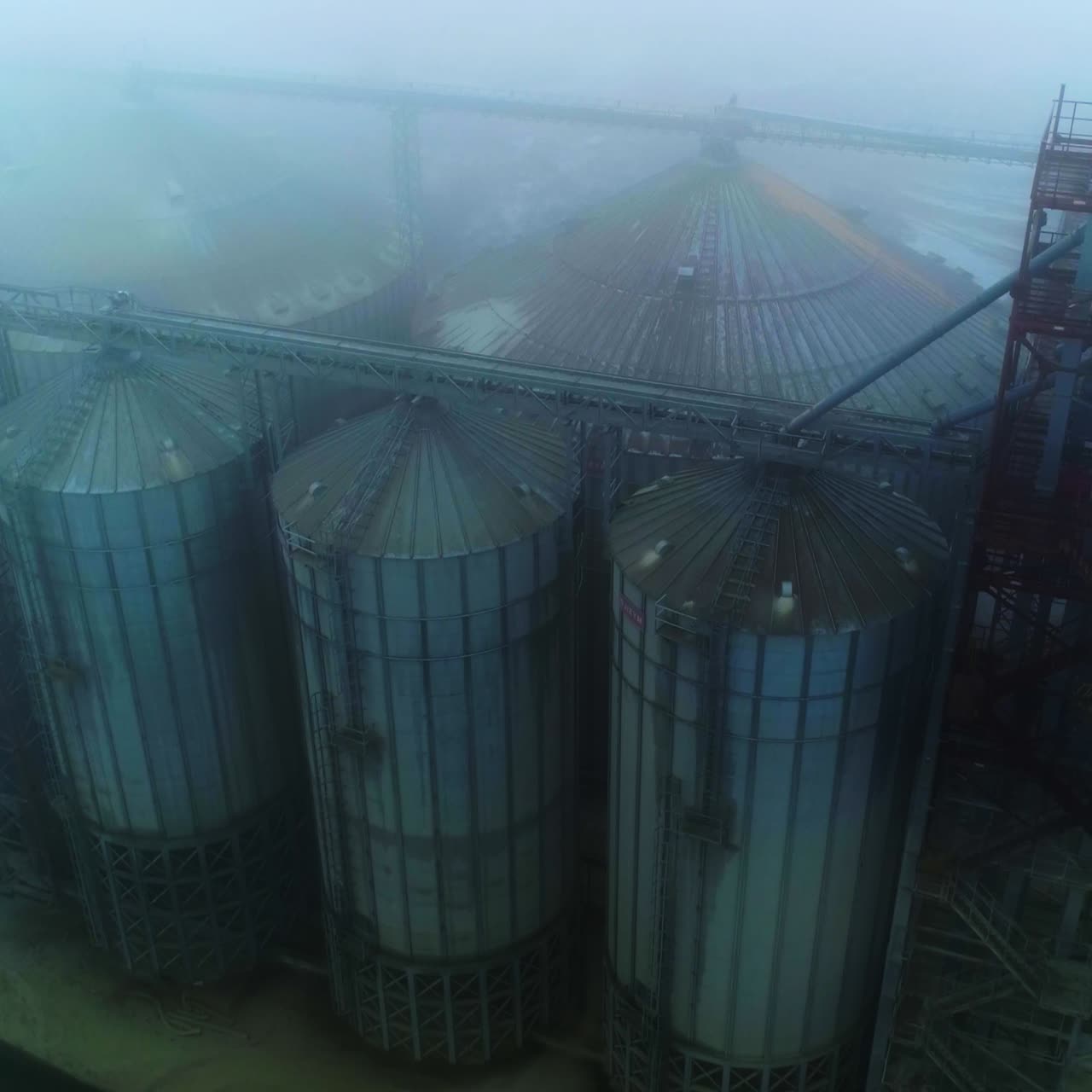 Gloomy sight of an agricultural granary plant. View from above on the modern elevator for grain storage. Foggy winter weather background