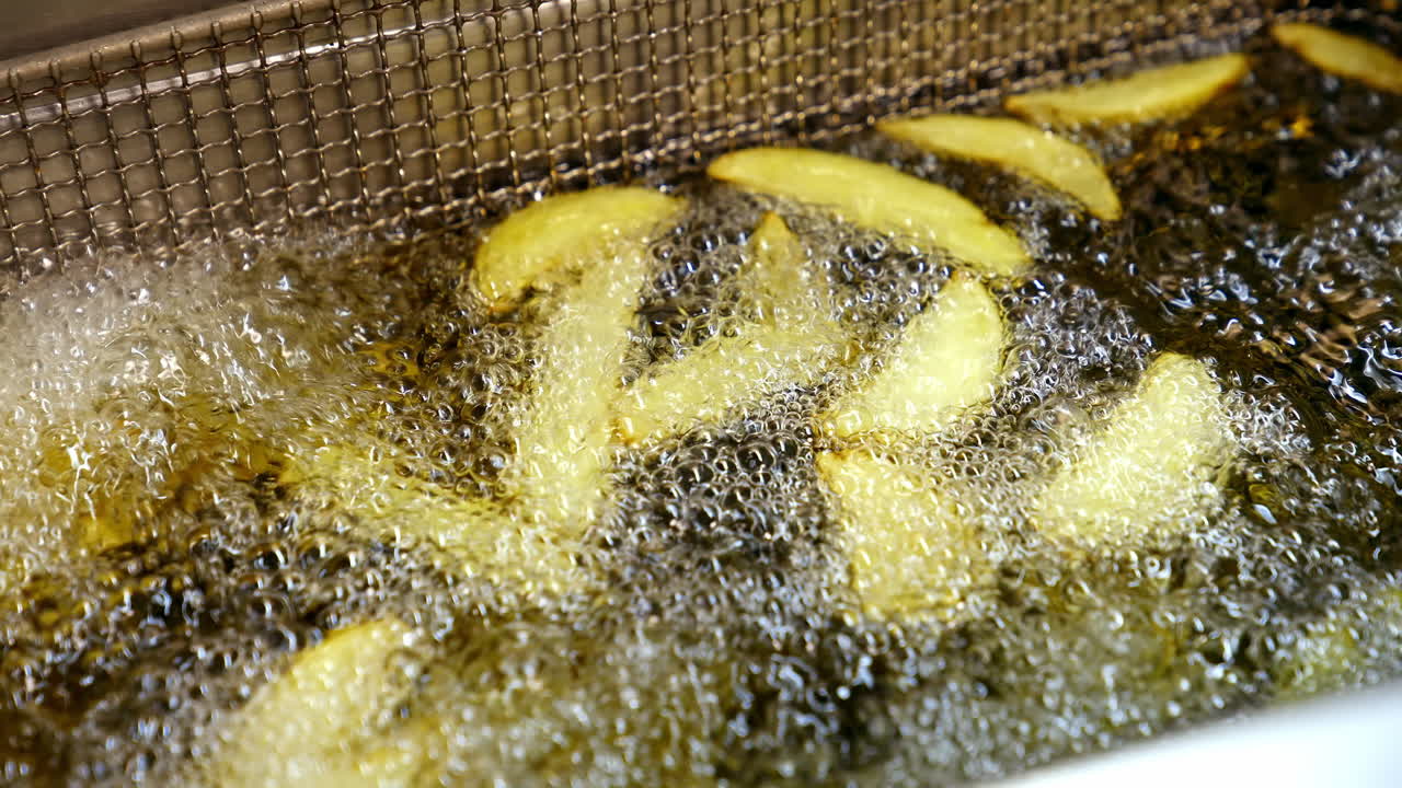 French fries prepared in a big quantity of oil in the deep fryer basket. Fast food restaurant concept.