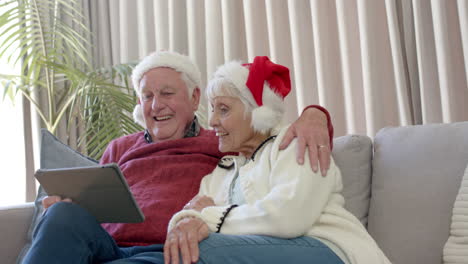 Pareja-Caucásica-Mayor-Con-Sombreros-De-Santa-Usando-Tableta-Para-Videollamadas-Navideñas,-Cámara-Lenta