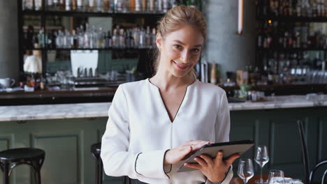 retrato de la propietaria de un bar de restaurantes de pie en el mostrador usando una tableta digital