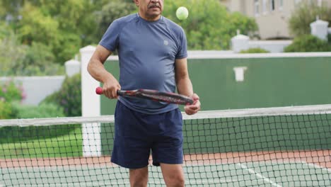 Vídeo-De-Un-Hombre-Mayor-Birracial-Feliz-Sosteniendo-Una-Raqueta-Y-Lanzando-Una-Pelota-En-Una-Cancha-De-Tenis