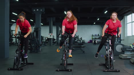healthy caucasian group of women exercising workout on stationary cycling machine bike in gym