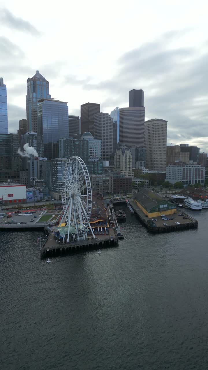 Panoramic vertical aerial view of coastal Giant Ferris wheel (Seattle Great Wheel) with cityscape backdrop along Seattle Waterfront, Washington, USA.