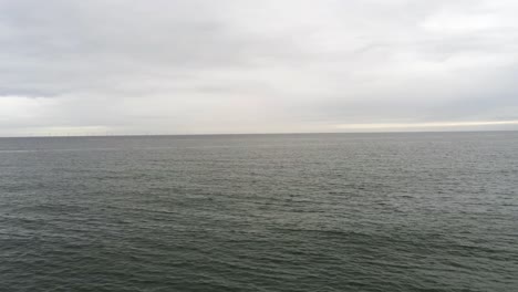 Ocean-horizon-reverse-pull-back-over-rocky-coast-boulders-shoreline