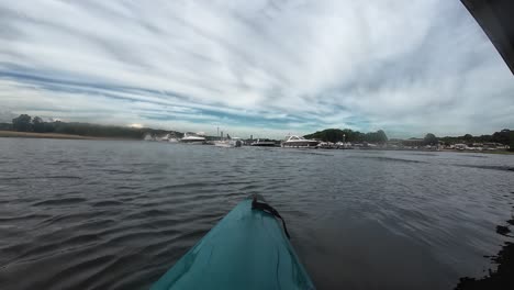 Kayaker under a bridge on Hamble River, England, with a blue kayak in focus. In the background, the marina and riverbank are visible, adding to the peaceful outdoor scene