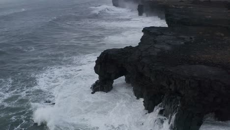 drone de arriba hacia abajo del agua golpeando un acantilado rocoso durante un día nublado en islandia