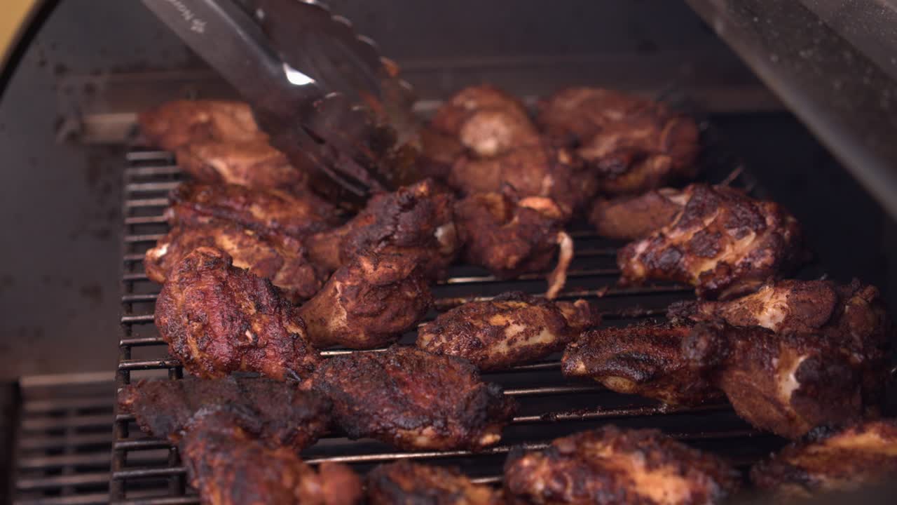 las alitas de pollo y los muslos en la parrilla de barbacoa caliente se giran con pinzas