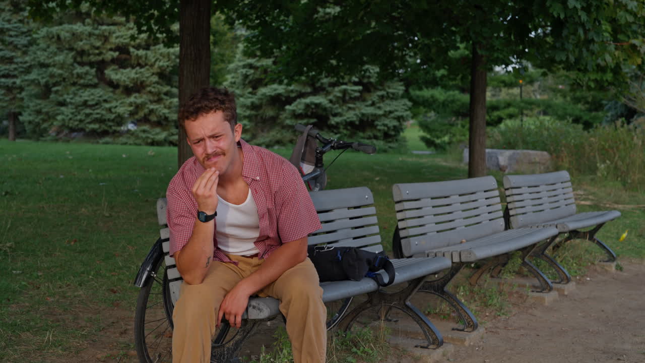 A young Gen Z man on a park bench receives a stressful phone message, reacts with frustration, and tosses his device into his backpack. Ideal for tech stress, burnout, and digital overload themes