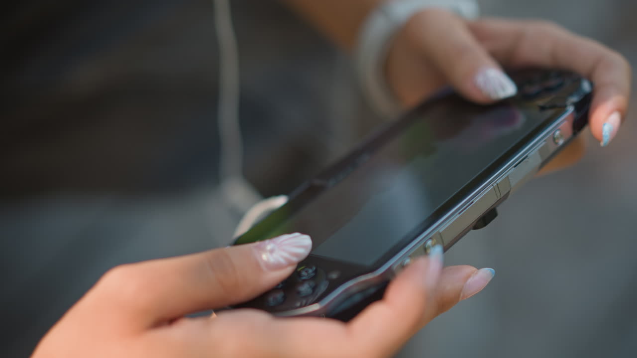 primer plano de unas manos en una videoconsola, uñas manicuradas y pulgar en el joystick, cable de los auriculares y reloj visibles, reflejos brillantes en la pantalla con manchas, toques precisos y destreza constante que demuestran control