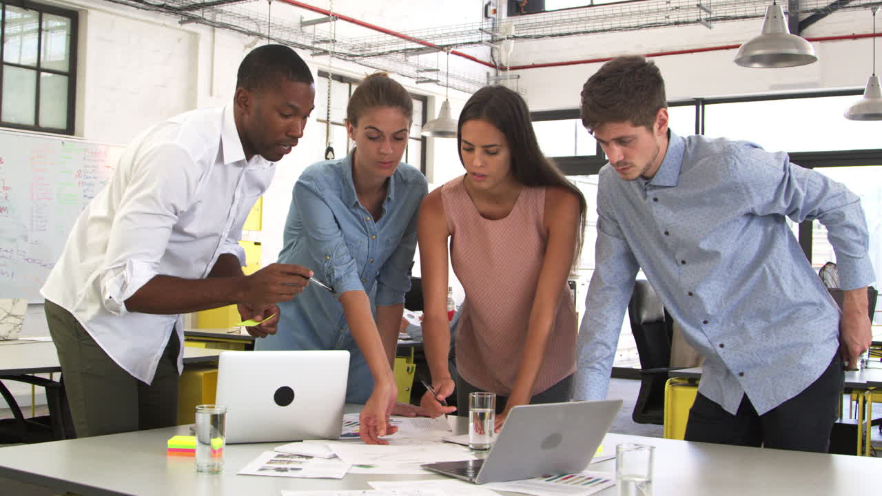 Four colleagues work standing at desk in an open plan office