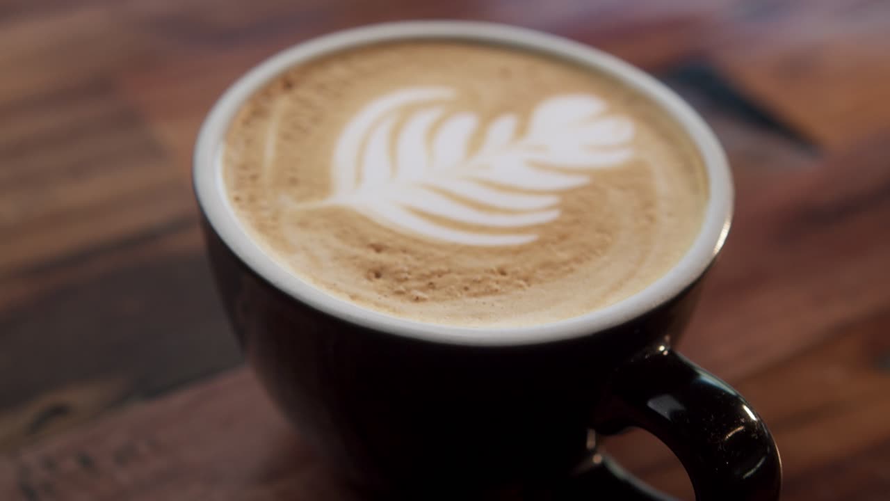 A leaf design is seen in the foam of a cup of coffee