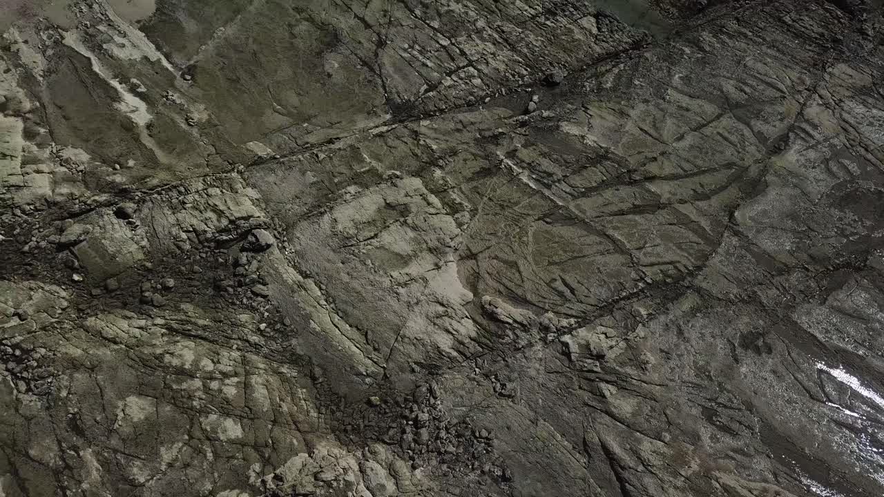 Interesting and Alternative Overhead Drone Shot of a Rocky Terrain with patches of shinny water that reflects the sun. Beach setting.