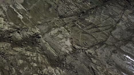 interesting and alternative overhead drone shot of a rocky terrain with patches of shinny water that reflects the sun. beach setting.