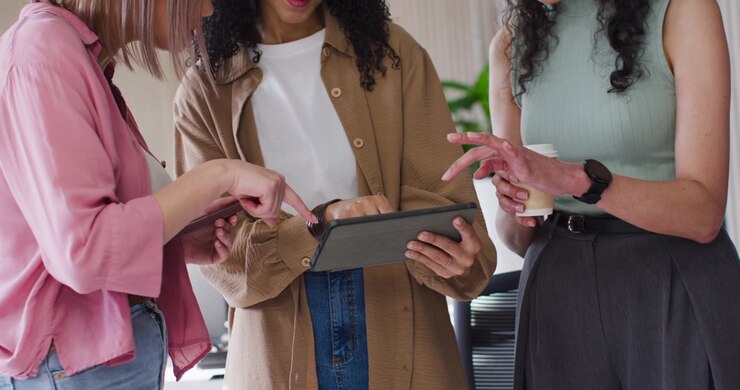 African American team meeting at tablet in office, woman tapping, peers pointing with phone and cup