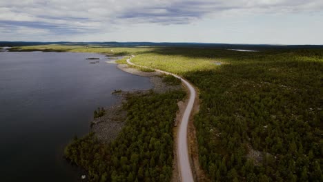 drone shot with lonely road between the green forest and calm lake