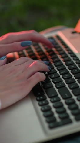 primer plano de una mujer escribiendo en una computadora portátil con uñas bien pulidas, reflejo cálido de la luz solar en el teclado y efecto de luz bokeh suave en el fondo