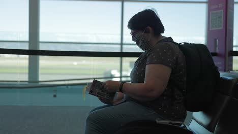 lady waiting ti board her flight reading a book in the airport waiting lounge
