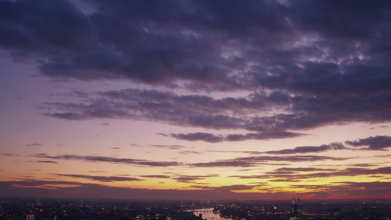 Aerial video shot at sunset captures a sprawling cityscape with a river, under a dramatic sky
