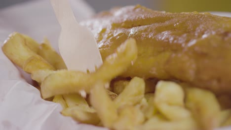 close-up von einer person, die eine traditionelle britische mahlzeit mit fisch und chips mit einer holzgabel isst