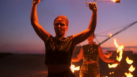 professional artists show a fire show at a summer festival on the sand in slow motion. fourth person acrobats from circus work with fire at night on the beach.