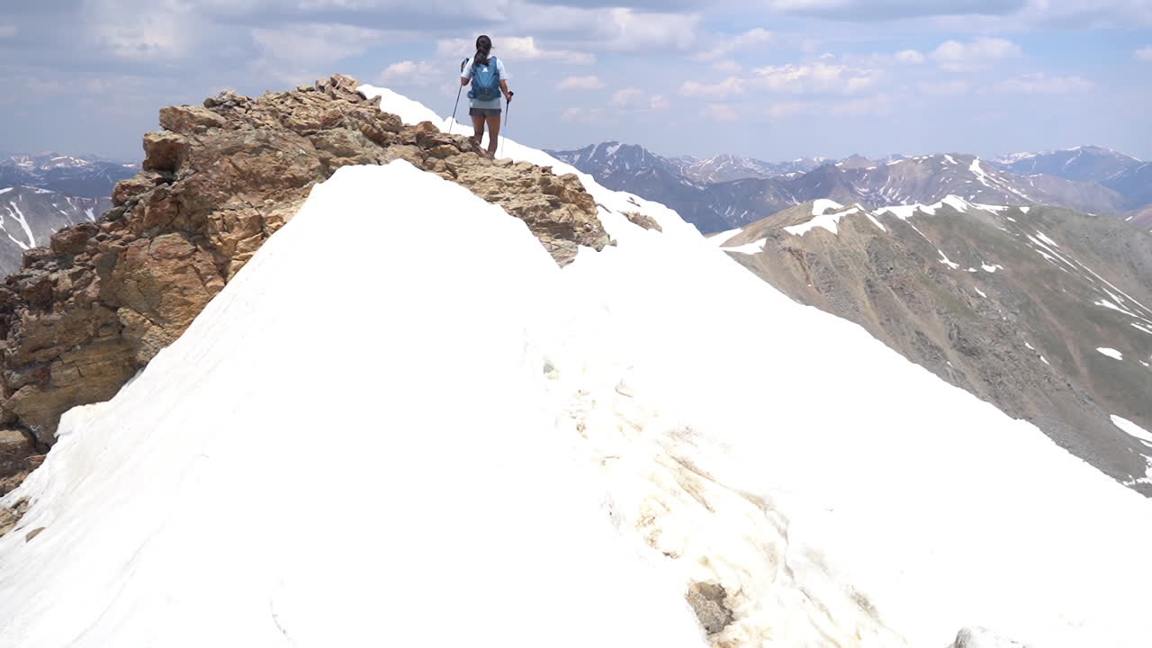 mujer montañera con bastones de trekking en la cumbre nevada con una vista increíble de la cordillera